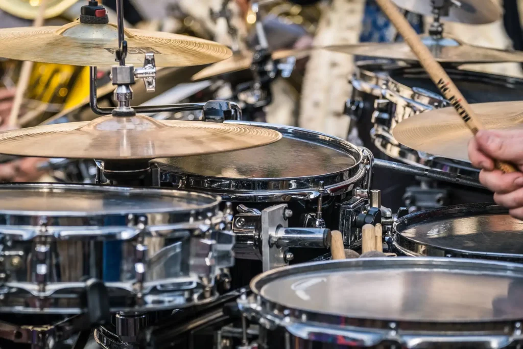 In the picture, a close-up of a person playing the drums: we can see the cymbals and a hand holding a drumstick.