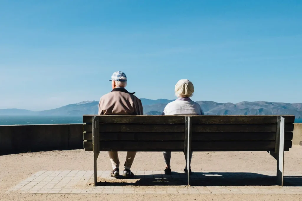 In the picture, an old couple sitting on a bench and looking at the view.